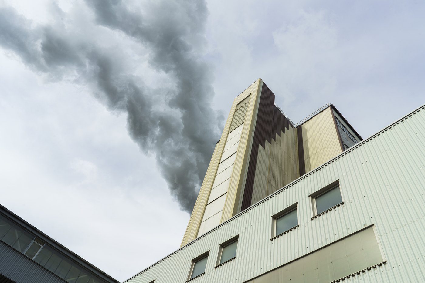 Looking up at a power-plant chimney venting dark smoke into a cloudy sky