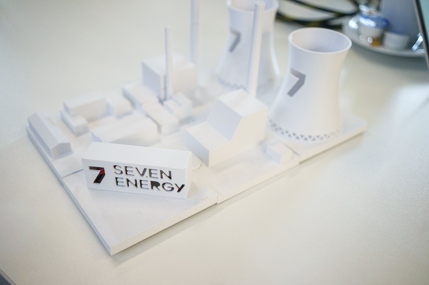 A close-up of the white architectural model, showing the '7 SEV.EN ENERGY' nameplate block beside the miniature cooling towers and plant buildings