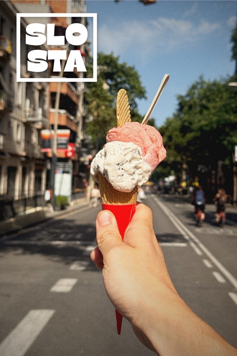 A film-look photo shot with SLOSTA — a hand holding a gelato cone on a sunlit Barcelona street, stamped with the SLO STA logo