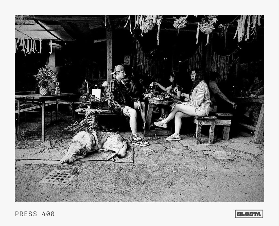 Two people at a bar table with a dog resting nearby, black-and-white film