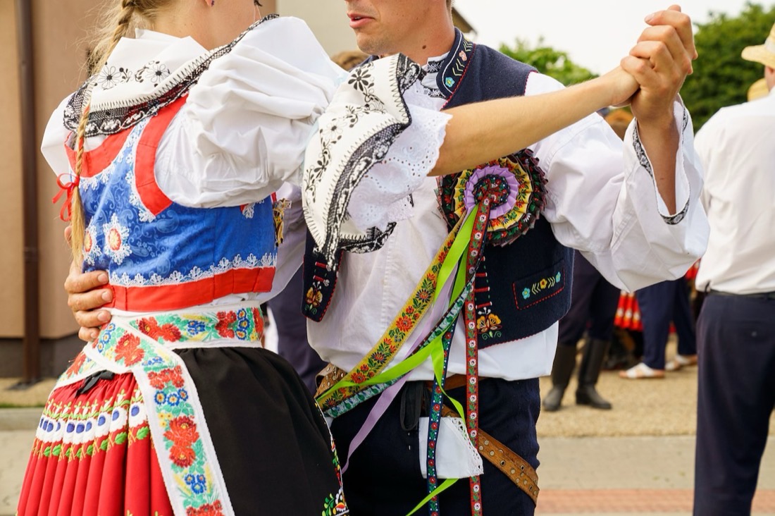 A couple dancing in detailed embroidered Moravian folk costume, ribbons trailing from the man's waistcoat